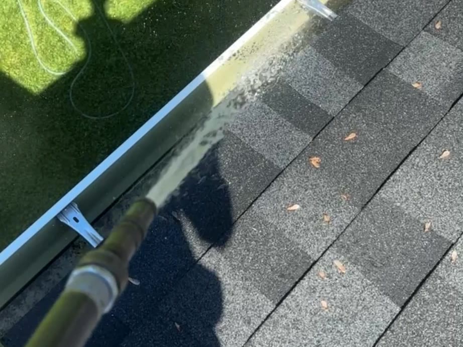 Flushing out a gutter trough from up on the roof, water running along the length of the gutter