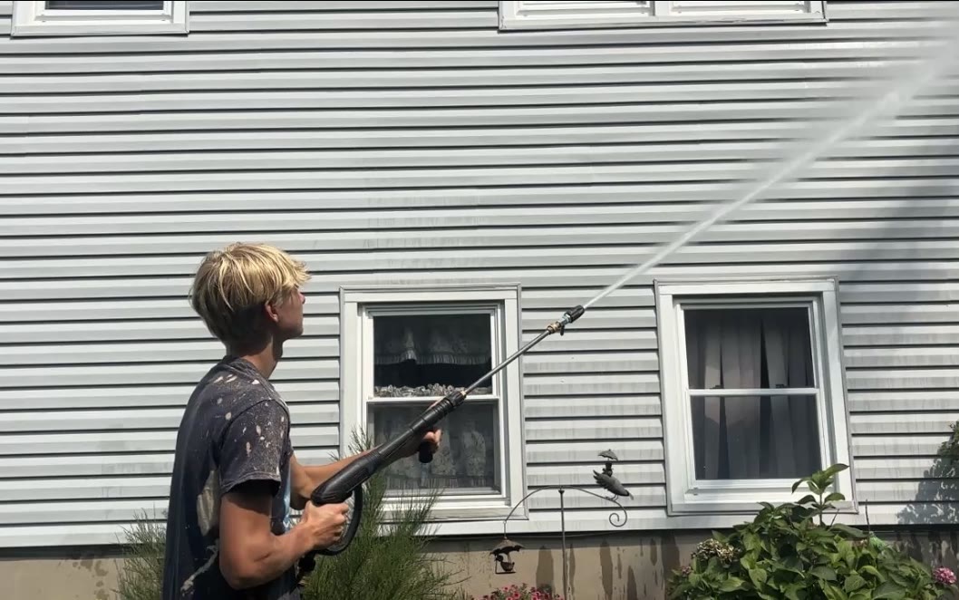 Daniel soft washing the siding of a two-story home, the spray arcing up across the wall